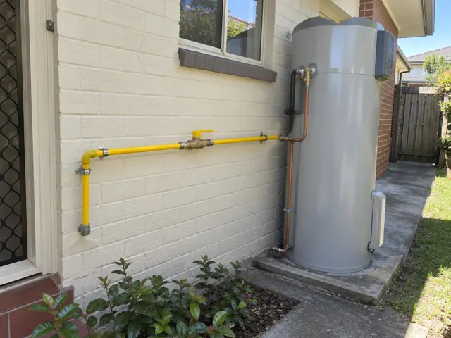 Yellow gas pipe and fittings on an exterior brick wall beside a cylinder in Eastgardens