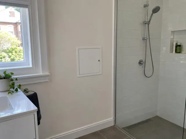 Bathroom wall with small access panel beside a tiled shower and vanity in Botany